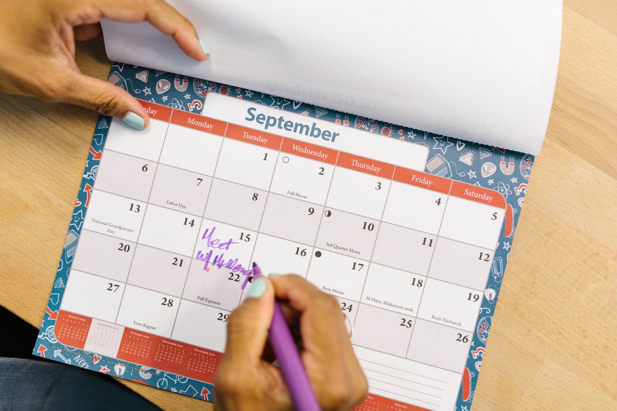 9月のカレンダーに、これからの予定をペンで書き込んでいる大人の手元
