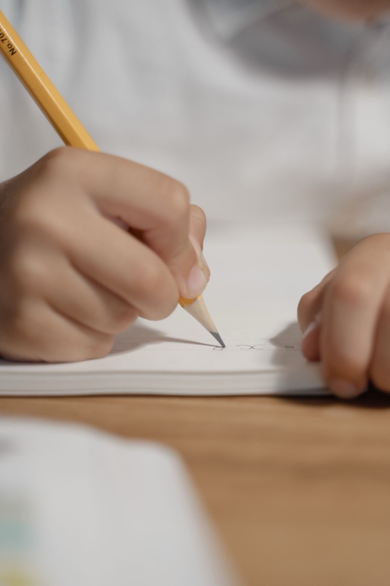 ノートに鉛筆で書き込む子どもの手元のクローズアップ。家で宿題に向かう時間が長くなりやすい