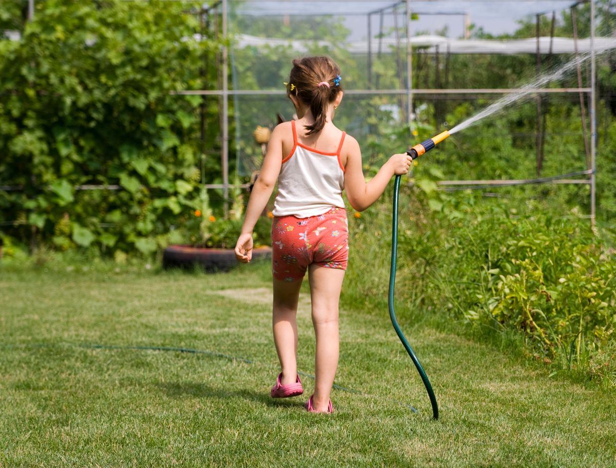 庭でホースの水を出して遊ぶ子どもの後ろ姿。強い感覚の刺激を自分から求めている場面のイメージ